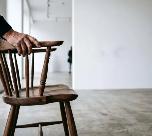 Artisan craftsperson examining traditional handmade furniture piece in minimalist contemporary gallery space